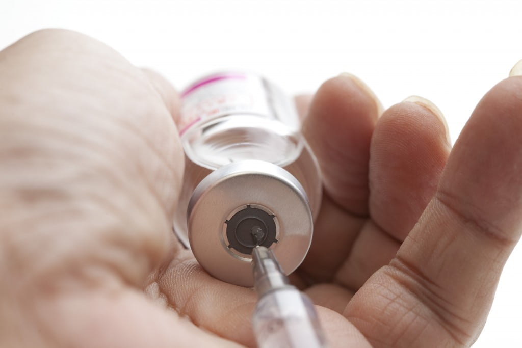 pharmacist immunisation: hands cupping vaccine bottle as needle draws fluid