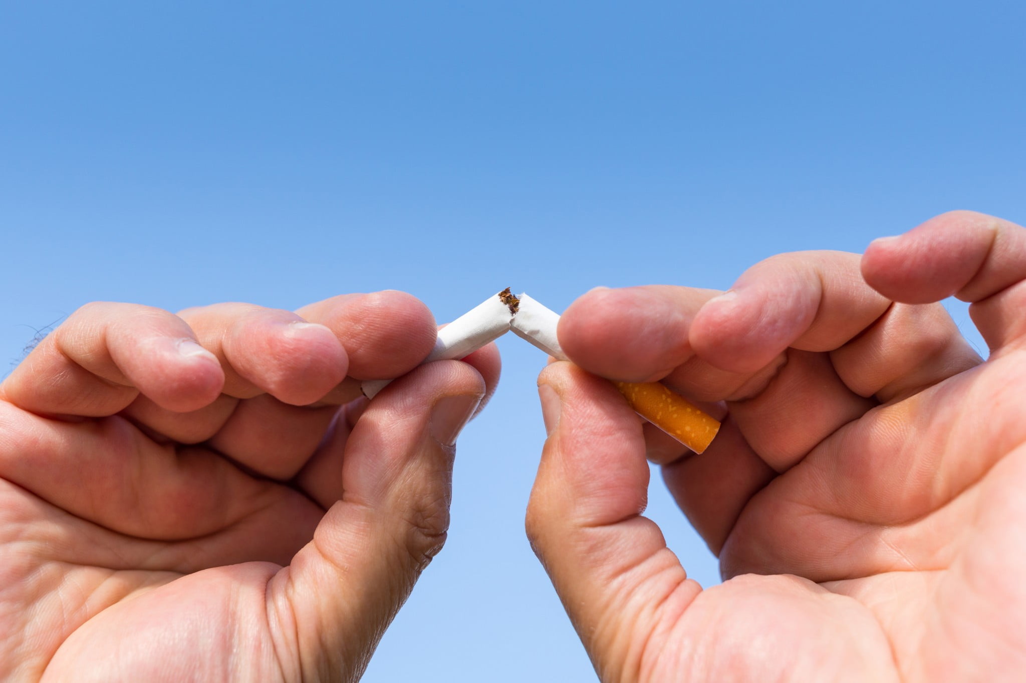 quit smoking: hands hold broken cigarette in front of blue sky