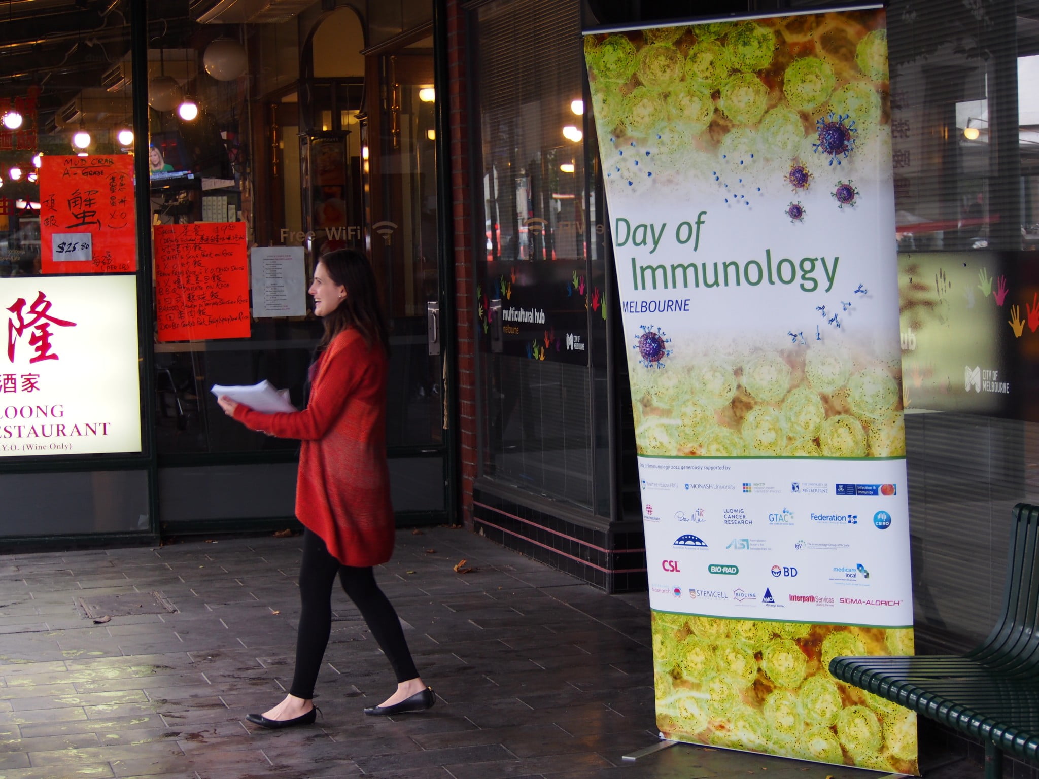 woman in red coat walks past the Vaccination Café sign