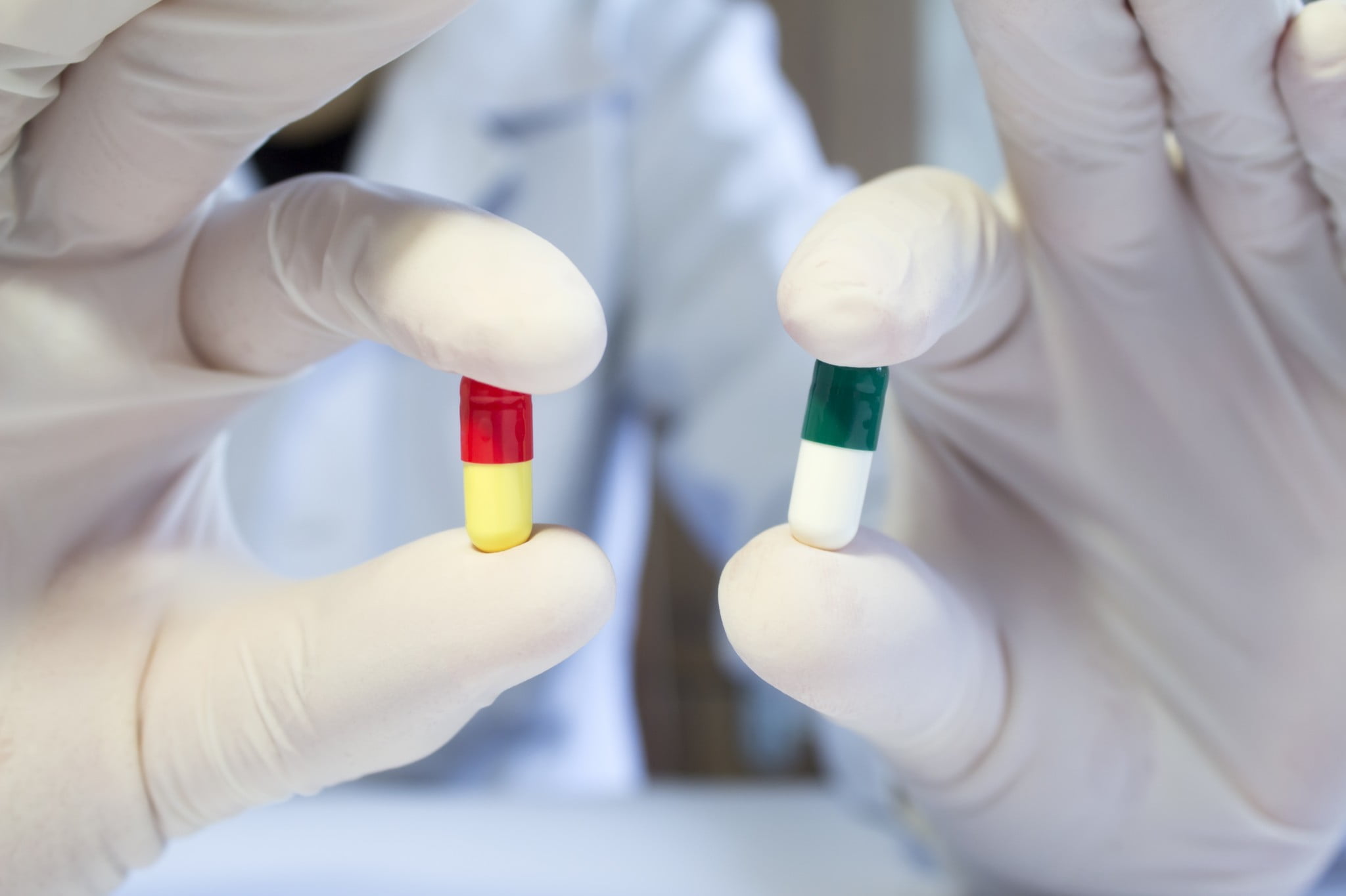 new antibiotics: gloved hands holding two antibiotic capsules