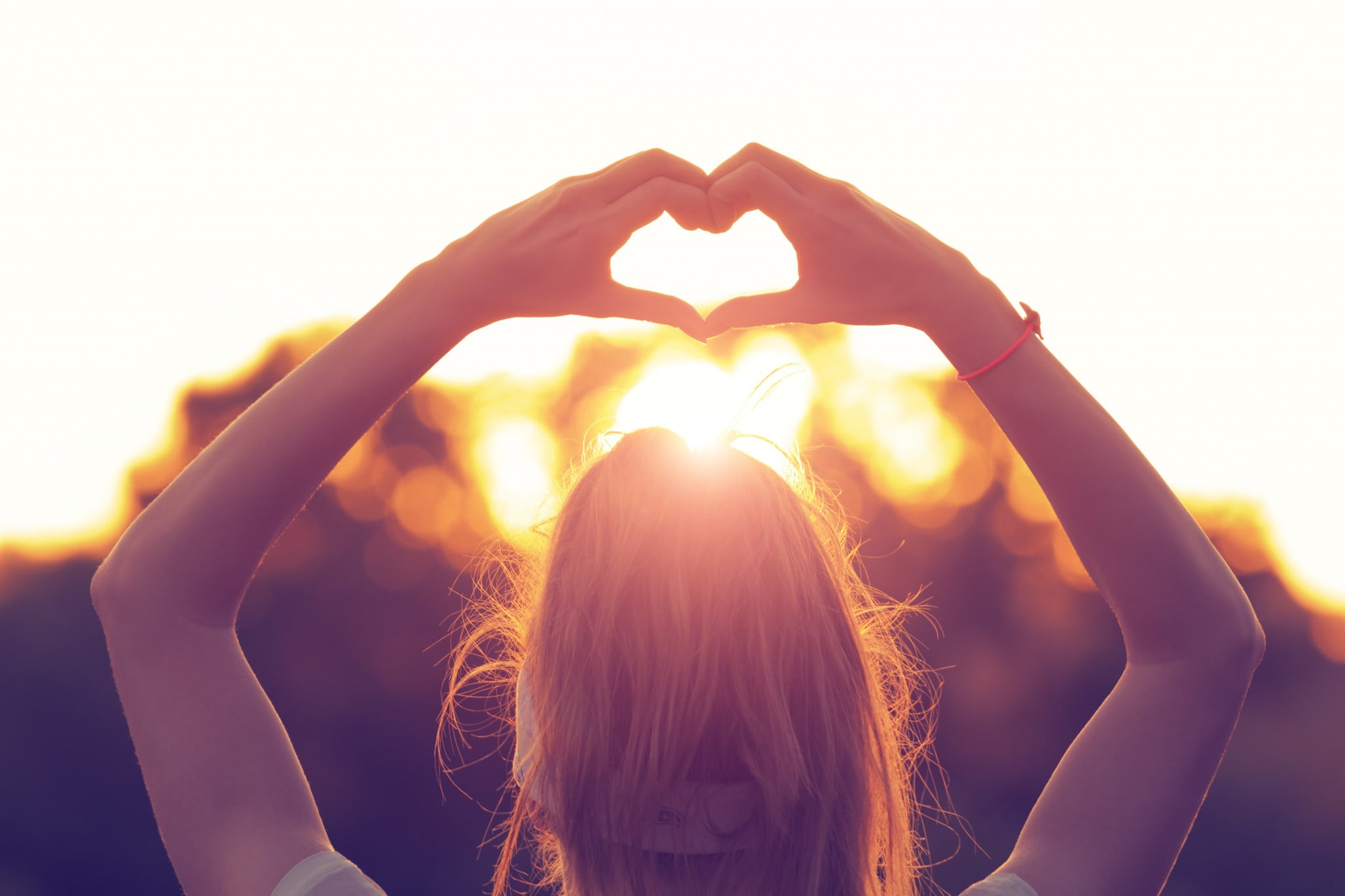 women's heart health: woman makes heart shape with hands backlit by sunset