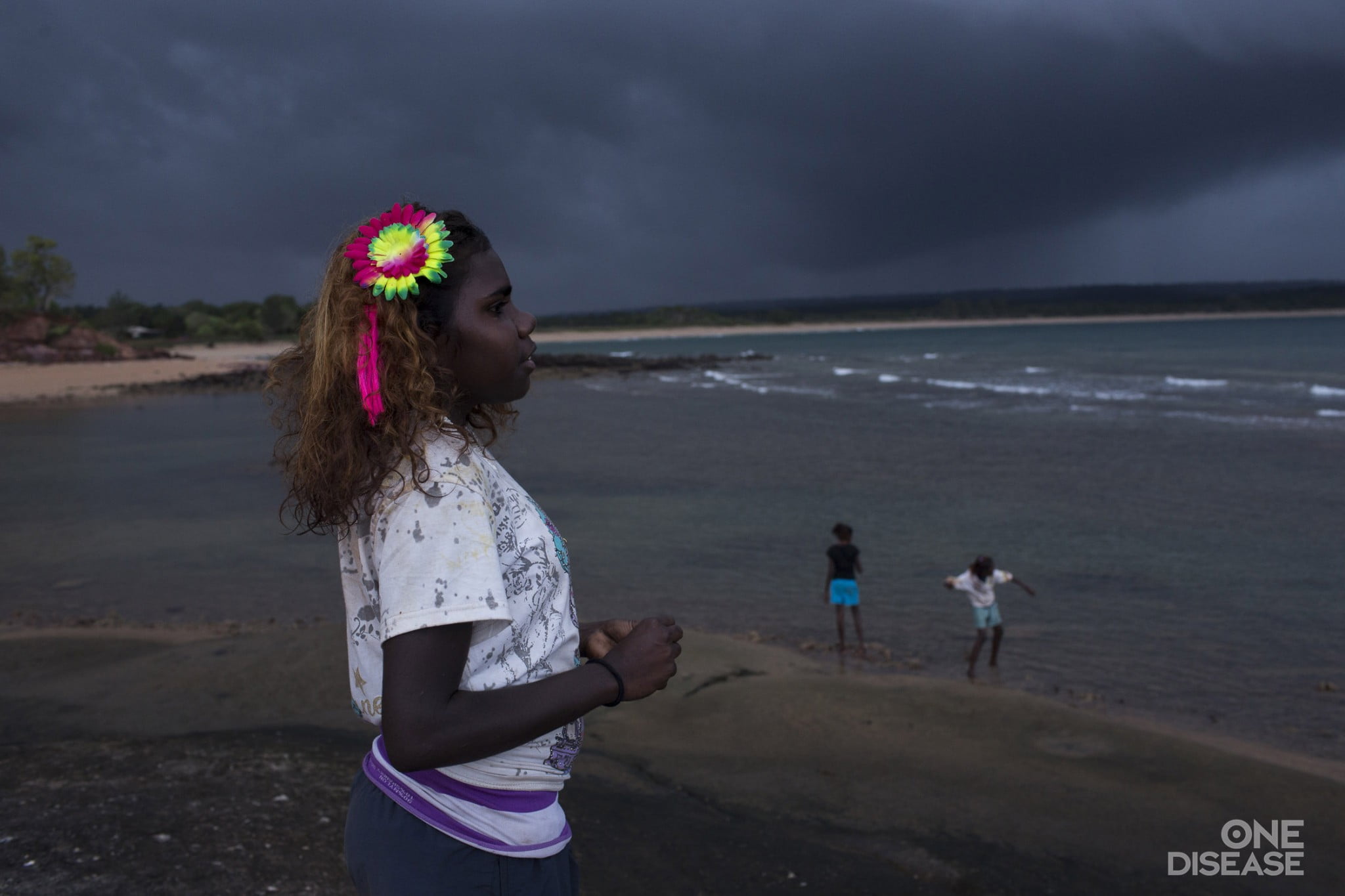 Young Aboriginal girl with bright flower in her hair looking out towards the ocean