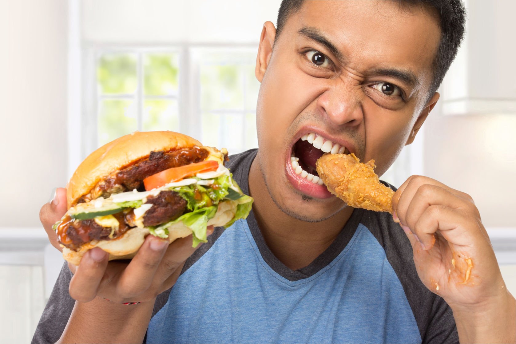 young man binge-eating a burger and drumstick