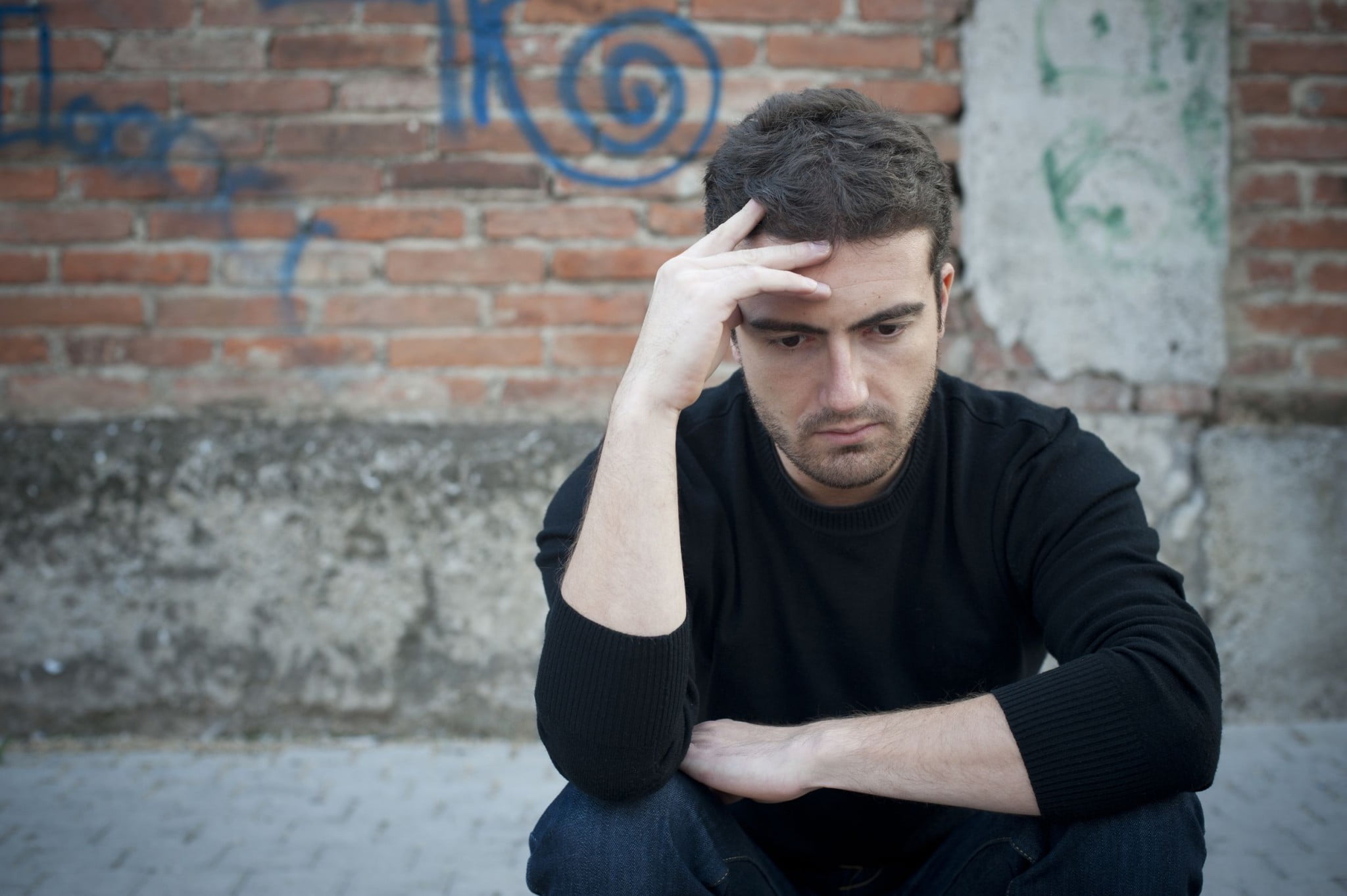 sad man in front of graffitied wall: harm minimisation story