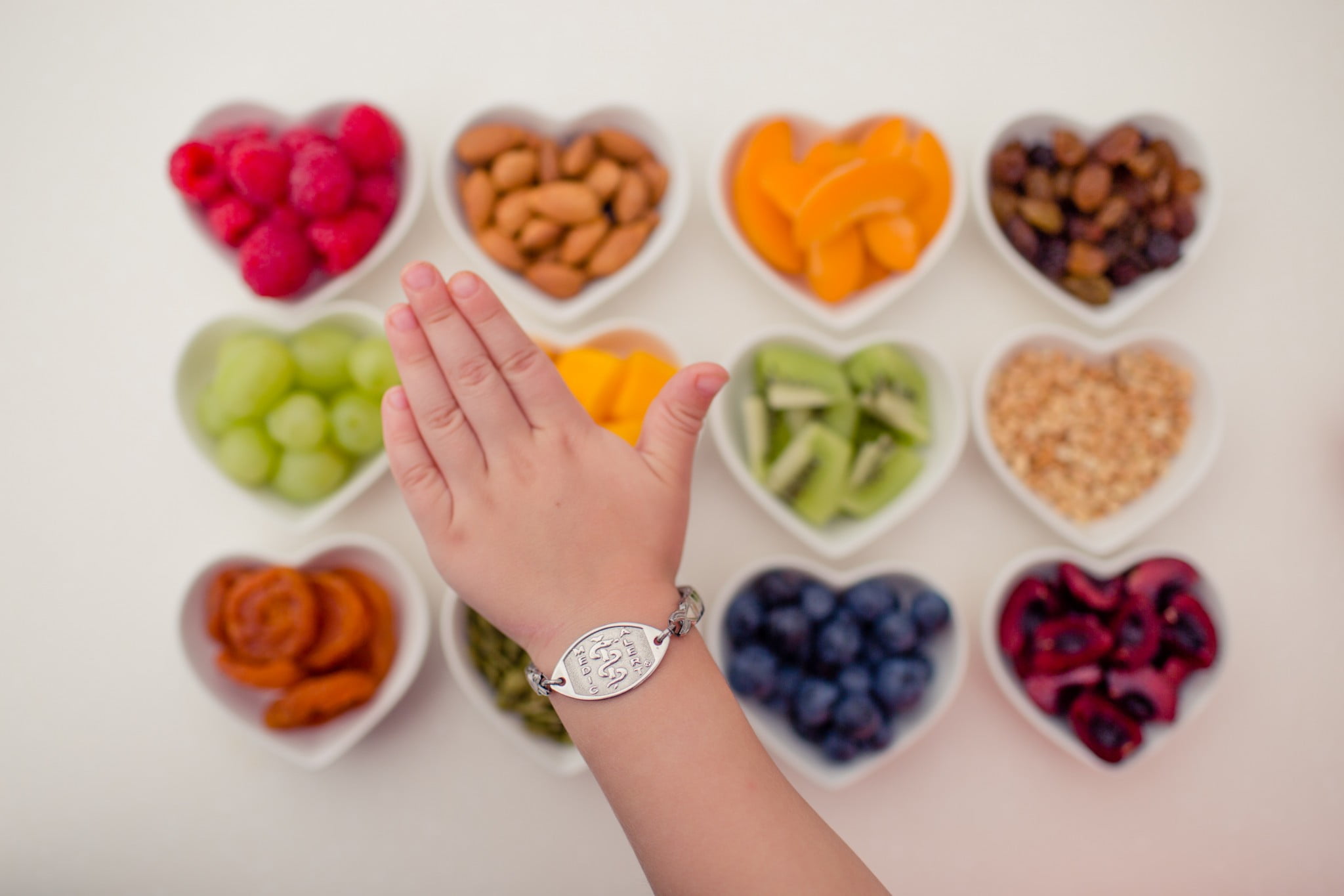 MedicAlert bracelet on wrist on background of food in heart shaped bowls
