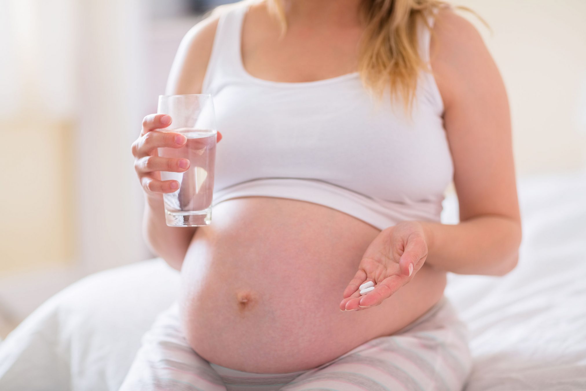 42325383 - pregnant woman sitting on bed and holding glass of water at home