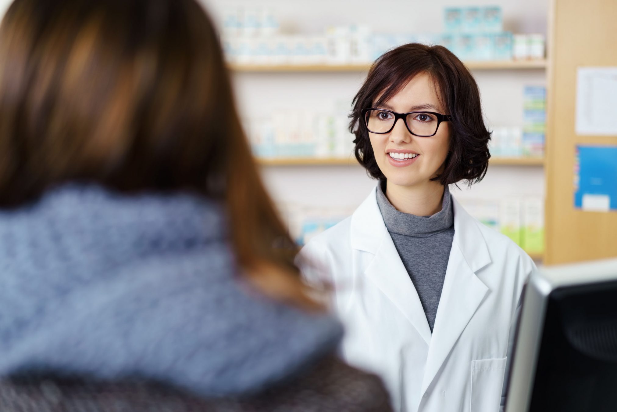 48653728 - young female pharmacist talking to a customer at the counter pleasantly.