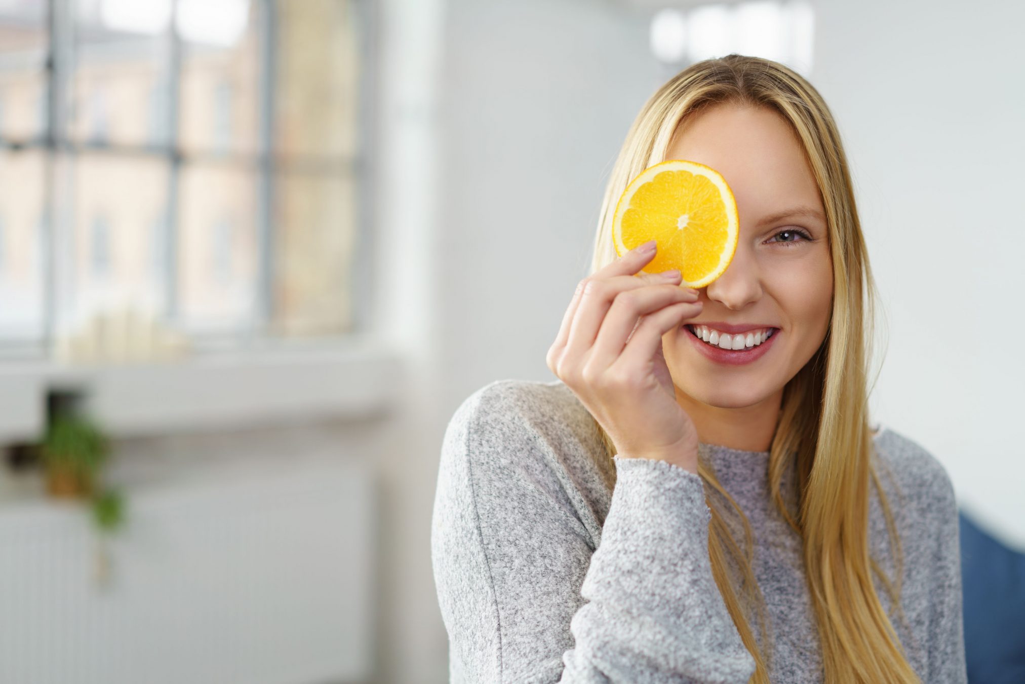 young woman holding slice of lemon to eye