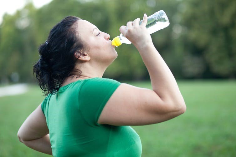 woman drinking bottle of water while exercising in park