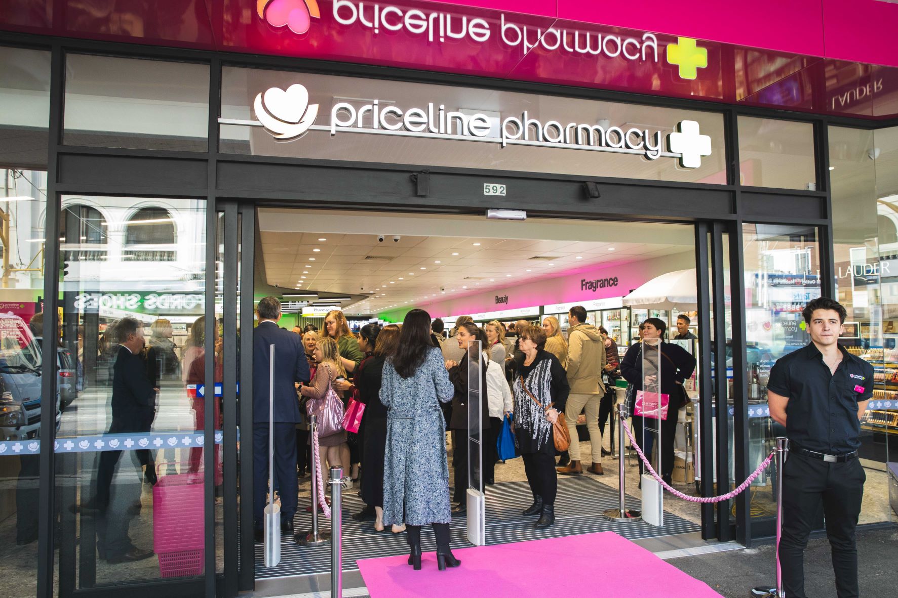 New Priceline store front with pink signage, many customers and pink carpet